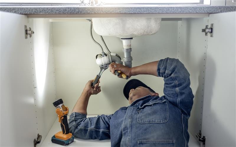 Plumber repairing pipes beneath a bathroom sink in Greenfield
