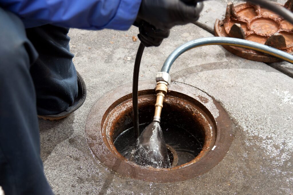 Plumber hydro jetting a sewer line through a manhole in Greenfield