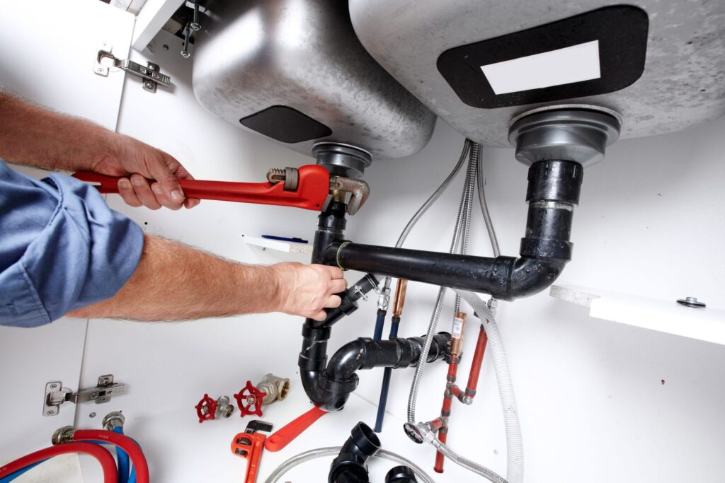 Plumber repairing drain pipes beneath a kitchen sink in Greenfield